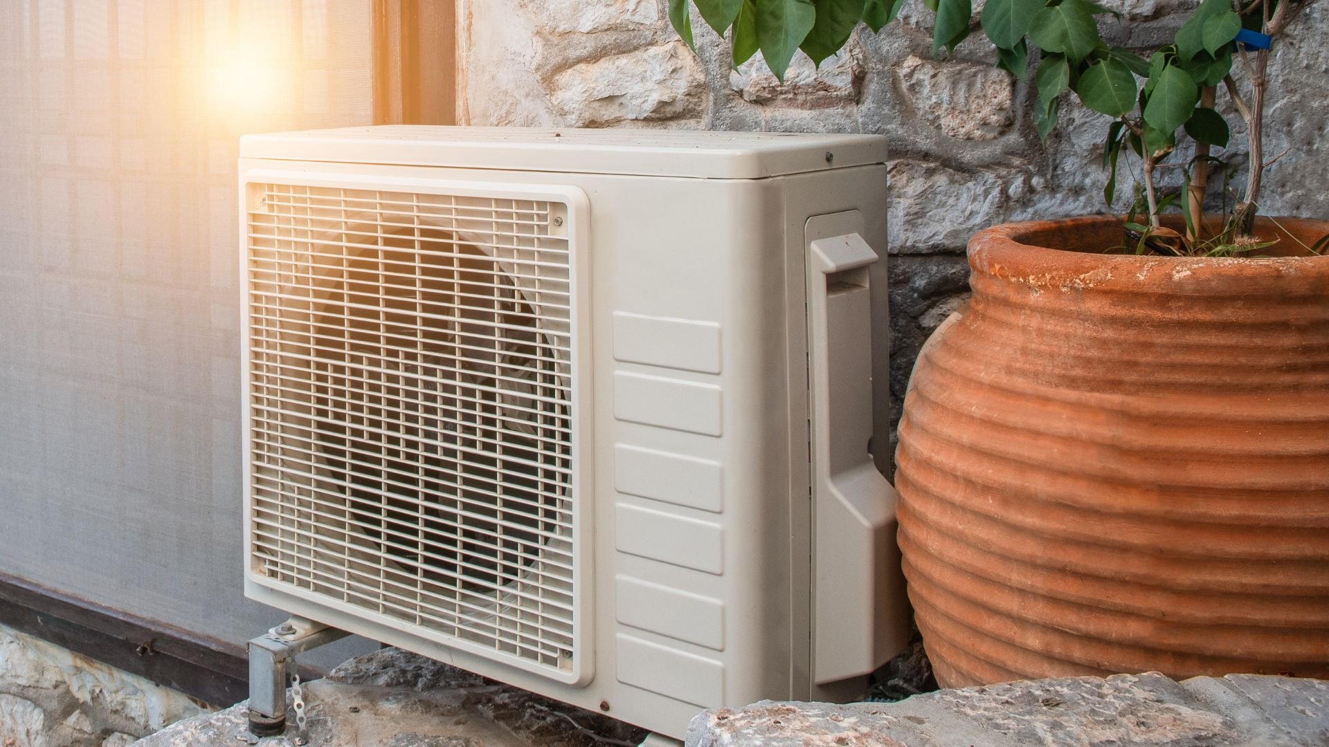 White air conditioning unit mounted on stone wall next to terracotta pot