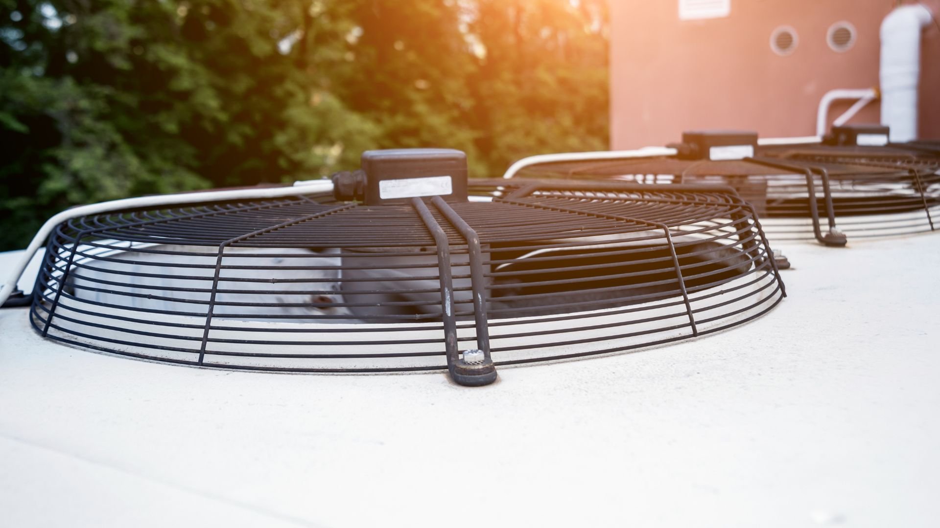 Industrial metal fan guards on rooftop with sunlight and trees